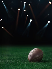 American football ball on a green grass on dark background and spotlight with laser rays