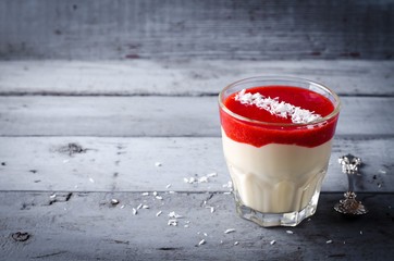 Creamy dessert with strawberry sauce and coconut flakes in glasses