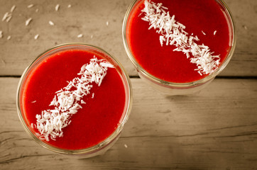 Creamy dessert with strawberry sauce and coconut flakes in glasses