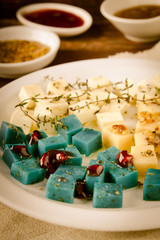 Cheese platter, Gouda, feta, blue pesto cheeses on white plate with herbs, olive oil, pomegranate and mustard sauces