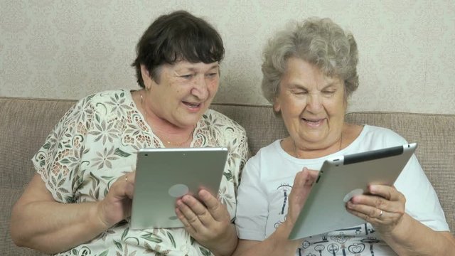 Two old women holding the silver digital tablets
