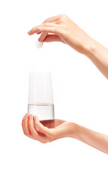 Hand holding white tablet over drinking glass with water