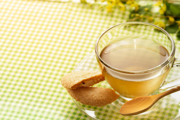 Glass cup of green tea with cookie on green fabric table.