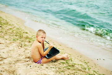 boy sitting with a laptop on the beach