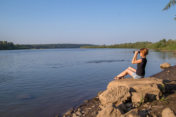 beautiful woman looking through binoculars while sitting on the shore
