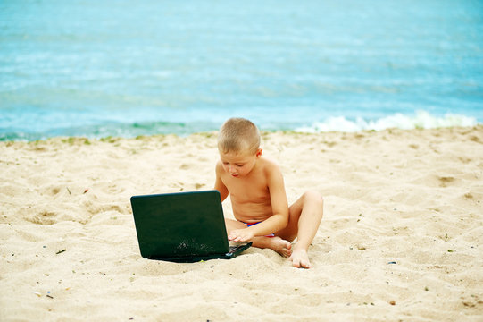 boy sitting with a laptop on the beach