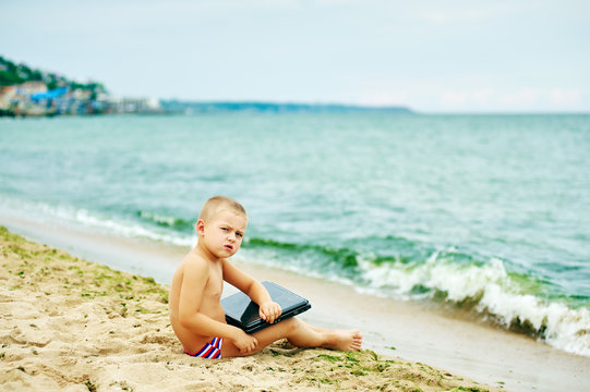 boy sitting with a laptop on the beach