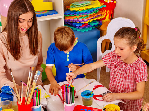 Children with teacher woman painting on paper at table in school. Painting school. Preschool children's development.
