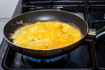 Scrambled eggs cooking in pan on gas flame