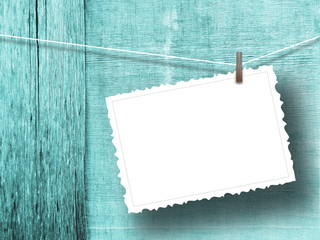 Close-up of one blank postcard frame hanged by peg against aqua weathered wooden boards background