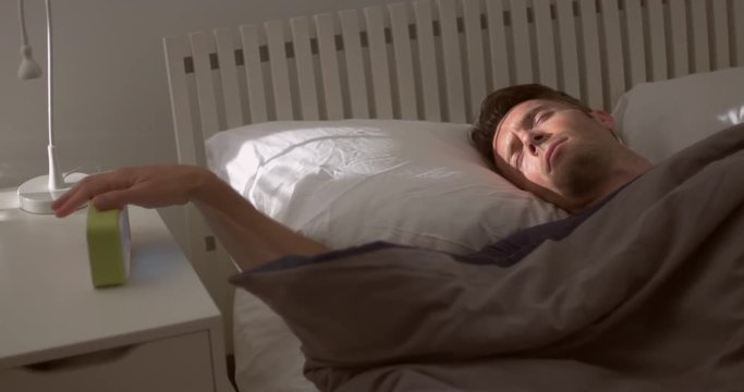 Man wakes up after oversleeping, leaps out of bed, grabs shirt, forgets trousers and doubles back for them.  Hand-held camera, medium shot.