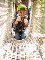 Teenager in helmet and with a safety rope sitting on a rope net and smiling