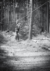 Toned image brave little boy in helmet and harness zip lining at adventure park on the background of pine trees