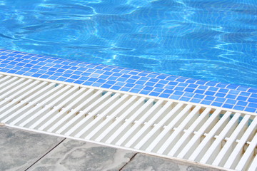 Swimming pool white grating grille with clear blue water and grey tiles.