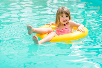 Fototapeta na wymiar Happy little girl floating in the pool to rescue circle yellow