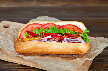 Big tasty hot dog with sauce and vegetables in parchment on the wooden background. hotdog gourmet.