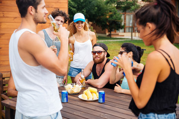 Happy young friends eating and drinking beer outdoors