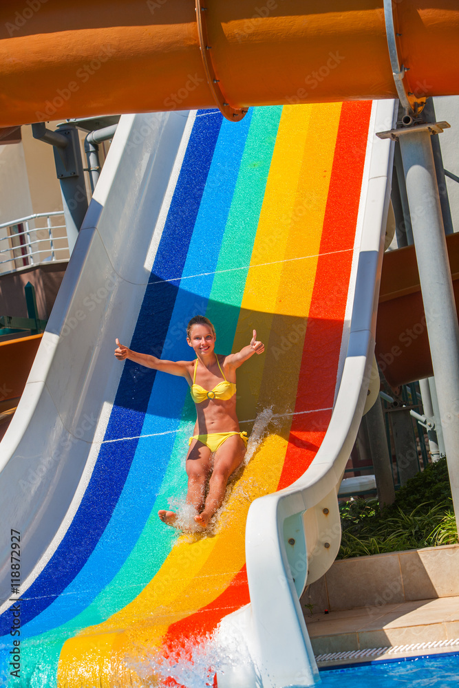 Wall mural Child on water striped slide atwater park show thumb up. Water slide with flowing water in water park. Summer water park holiday. Outdoor.