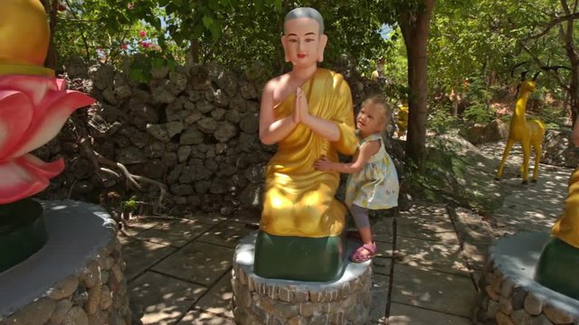 Little Girl Plays at Sitting Buddha Statues in Temple Park