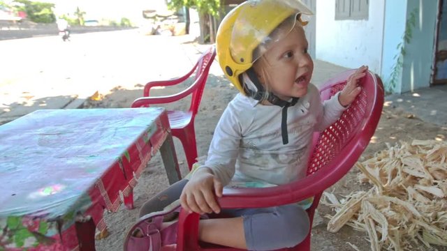 Little Girl in Helmet Sits on Chair at Table in Sideroad Cafe
