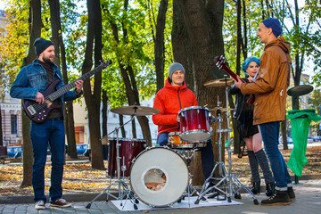Music street performers with girl violinist on autumn outdoor. Group people three men and women with music instrument in park.