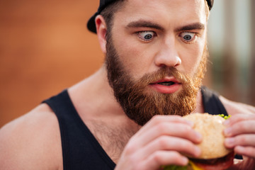 Amazed shocked young man holding and looking at hamburger outdoors