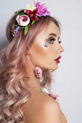Naklejka premium Pretty young woman with Wreath of Pink Flowers. Beauty fashion model girl with long curly hair and colorful make-up isolated on white/grey background