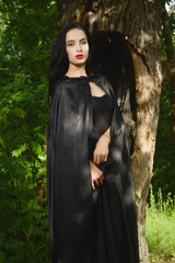 Beautiful brunette woman in black dress and black cloak in the m