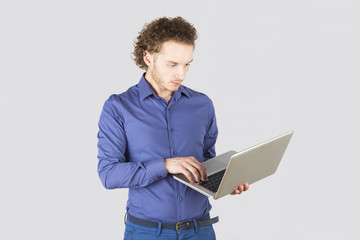 Smart man typing something on laptop in studio on gray background. Modern lifestyle.
