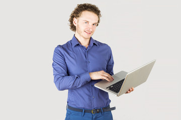 Handsome man with laptop in hands in studio on gray background. Modern lifestyle.