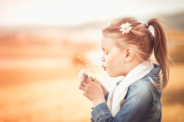 Little beautiful girl blow a dandelion in the summer light