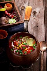 Tomatoe mexican soup with spices and lime on wooden table