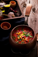 Tomatoe mexican soup with spices on wooden table.