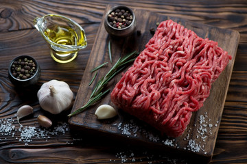 Raw fresh ground meat with seasonings in a rustic wooden setting