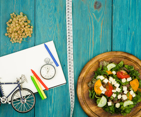bicycle model, salad of fresh vegetables, notepad, stopwatch and tape measure on a blue wooden table