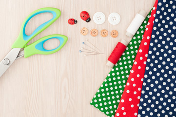 Fototapeta premium Fabric for sewing and accessories for needlework on wooden background. Spool of thread, scissors, buttons, sewing supplies