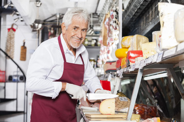 Fototapeta na wymiar Happy Salesman Slicing Cheese In Shop