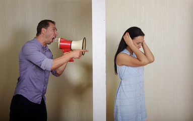 Man shouts at woman through a megaphone, she covers her ears with the hands. Conflict concept