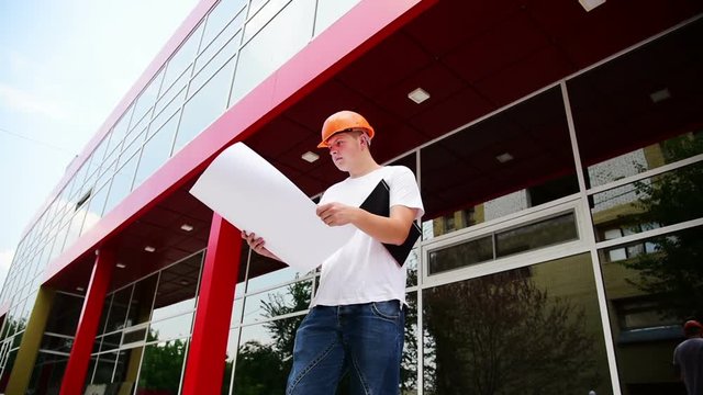 The civil engineer checks the building plan. The man the builder in a helmet and a white t-shirt. Work on the building site.