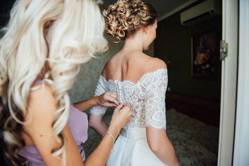 Fototapeta na wymiar bridesmaids help to wear a wedding lace dress