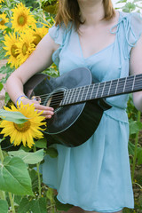 Mujer joven con un vestido de verano tocando la guitarra en un campo de girasoles