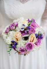 Wedding bouquet made of violet flowers and beige roses held by g