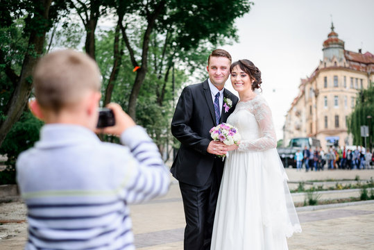 Little boy takes a picture of pretty wedding couple