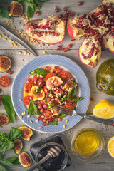 Fruit salad with fig on the ceramic plate with ingredients on the white wooden table vertical