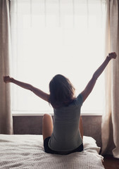 Happy young woman stretching in bed after waking up, back view