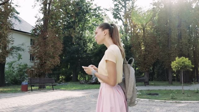 Young slim woman in pink skirt and yellow t-shirt uses the navigation on smart phone and go in the direction indicated