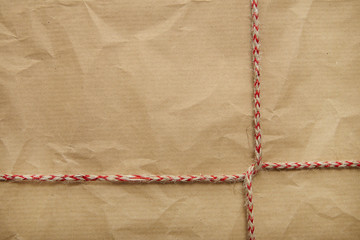 A full page of creased brown parcel paper texture with red striped string tied around it