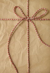 Fototapeta na wymiar A full page of creased brown parcel paper texture with red string bow tied around it