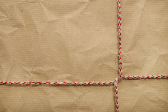 A full page of creased brown parcel paper texture with red striped string tied around it