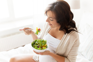 happy pregnant woman eating salad at home